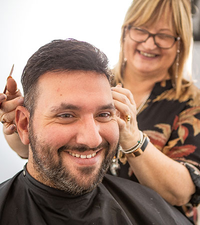 Woman giving a haircut to a smiling man with a bonded topper